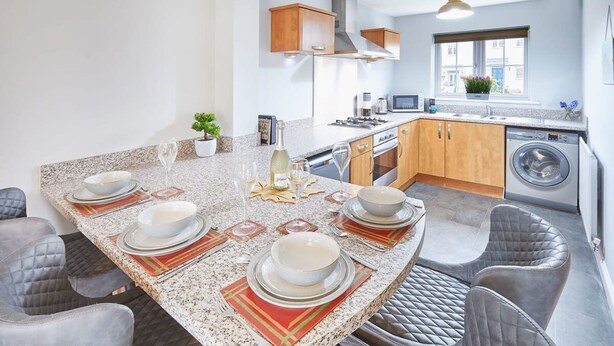 A modern kitchen with granite countertops, wooden cabinets, a built-in oven, microwave, and a washing machine.