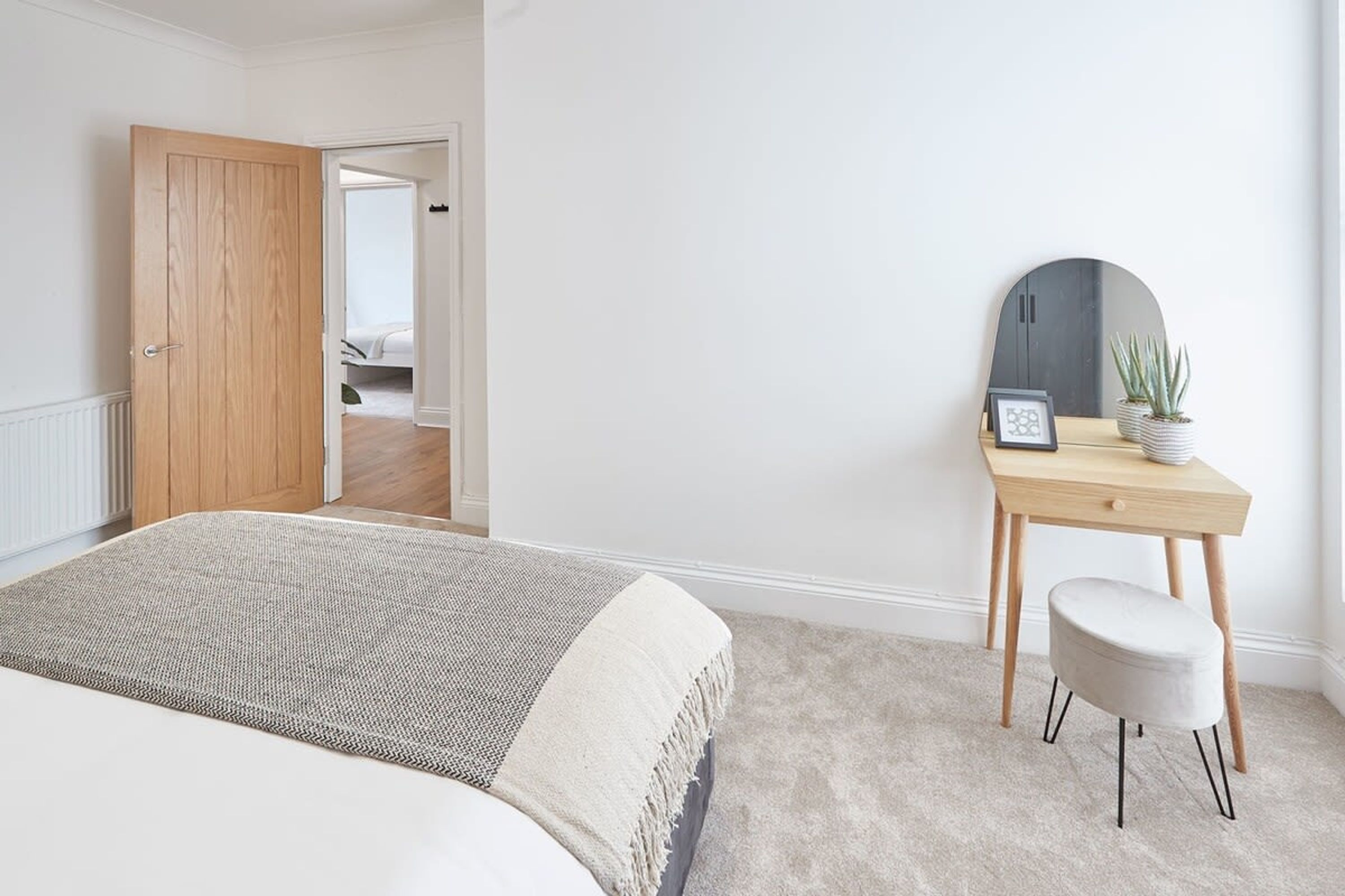 A bedroom with a bed, a desk with a mirror, and a small stool.