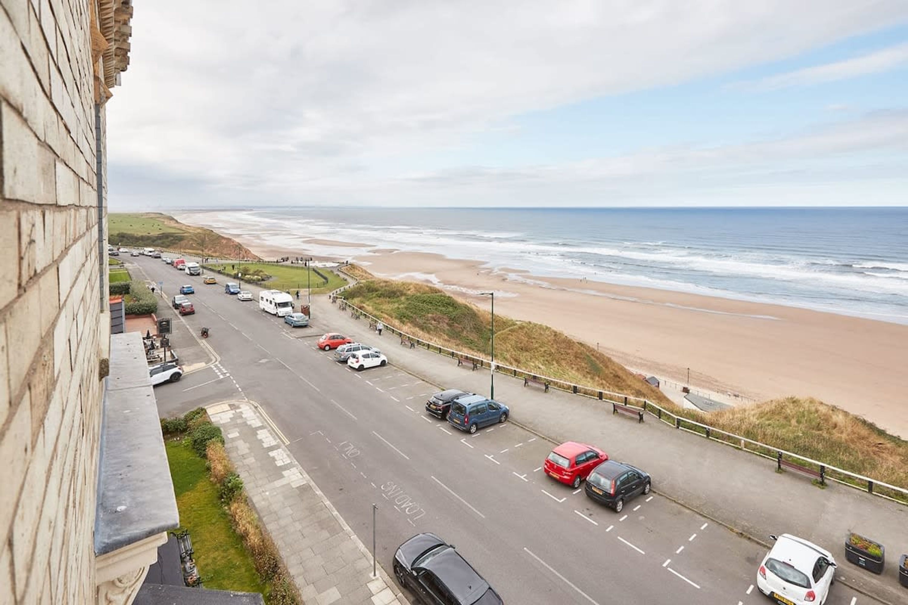 A coastal road with vehicles, a beach, and a building on the left.