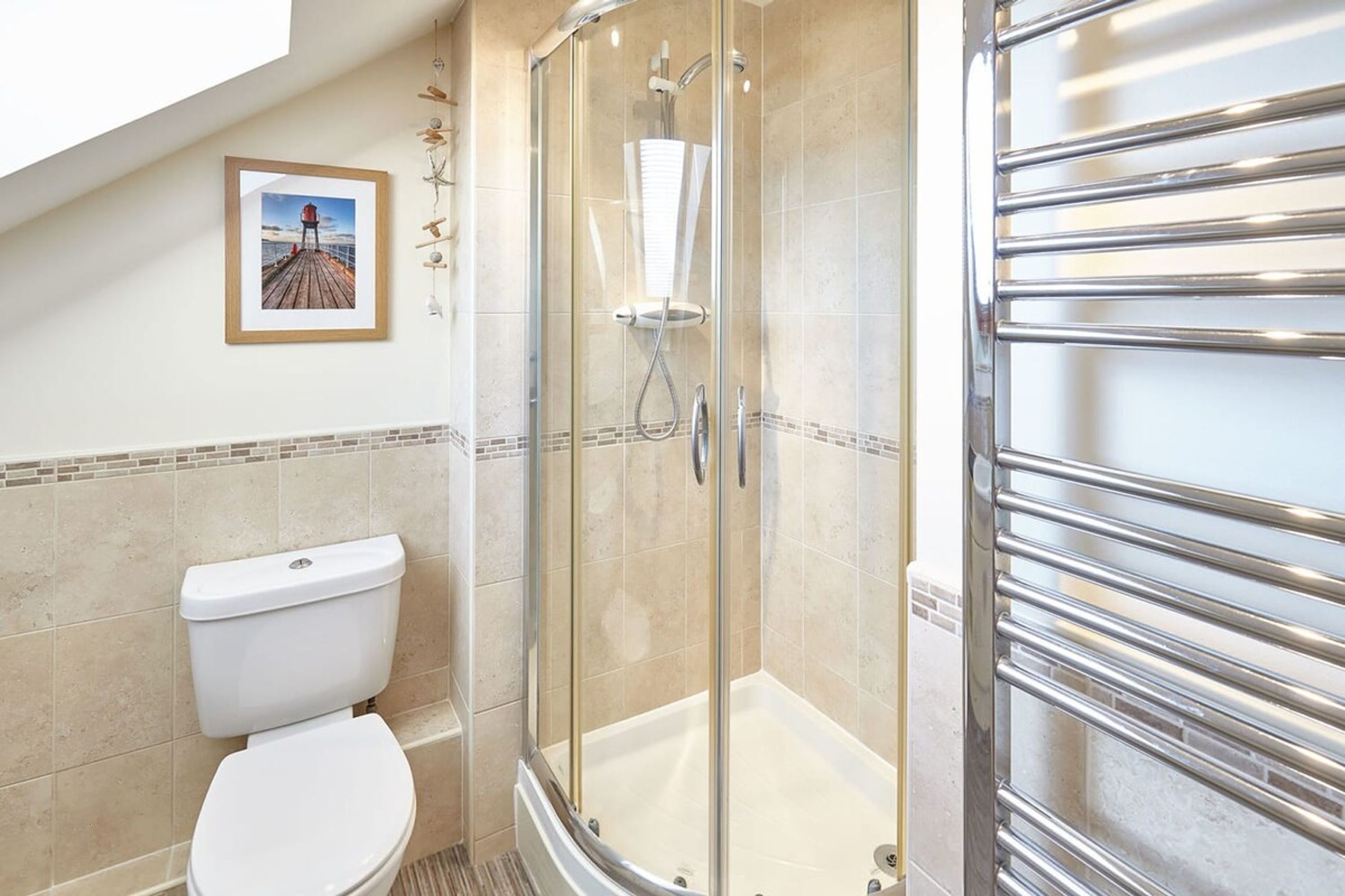 Une salle de bain avec une douche à parois de verre, des toilettes blanches et un tableau encadré au mur.