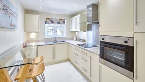 A modern kitchen with white cabinets, a stainless steel oven, and a glass dining table with chairs. - Host Stay Abbey Horizon (Whitby)