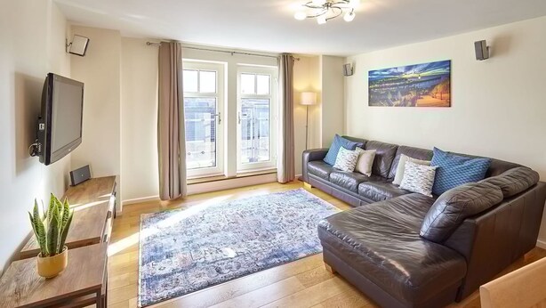 A modern living room with a large sofa, a flat-screen TV, a dining table, and a view through large windows. - Host Stay Abbey Horizon (Whitby)