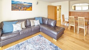 A living room with a leather sofa, a dining table with chairs, a large painting on the wall, and a wooden floor. - Host Stay Abbey Horizon (Whitby)
