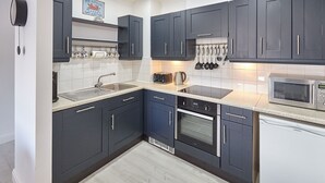 Une cuisine moderne avec des meubles de couleur sombre, un four à micro-ondes en acier inoxydable, un four encastré et une machine à café.