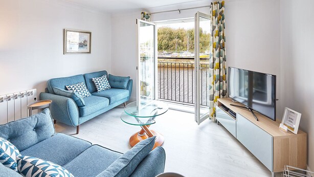 Un salon moderne avec un canapé, une table basse en verre, un téléviseur et une vue sur une rivière, visible à travers une porte coulissante.