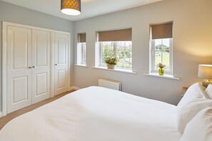 A bedroom with a large bed, two windows with curtains, a radiator, and a door.