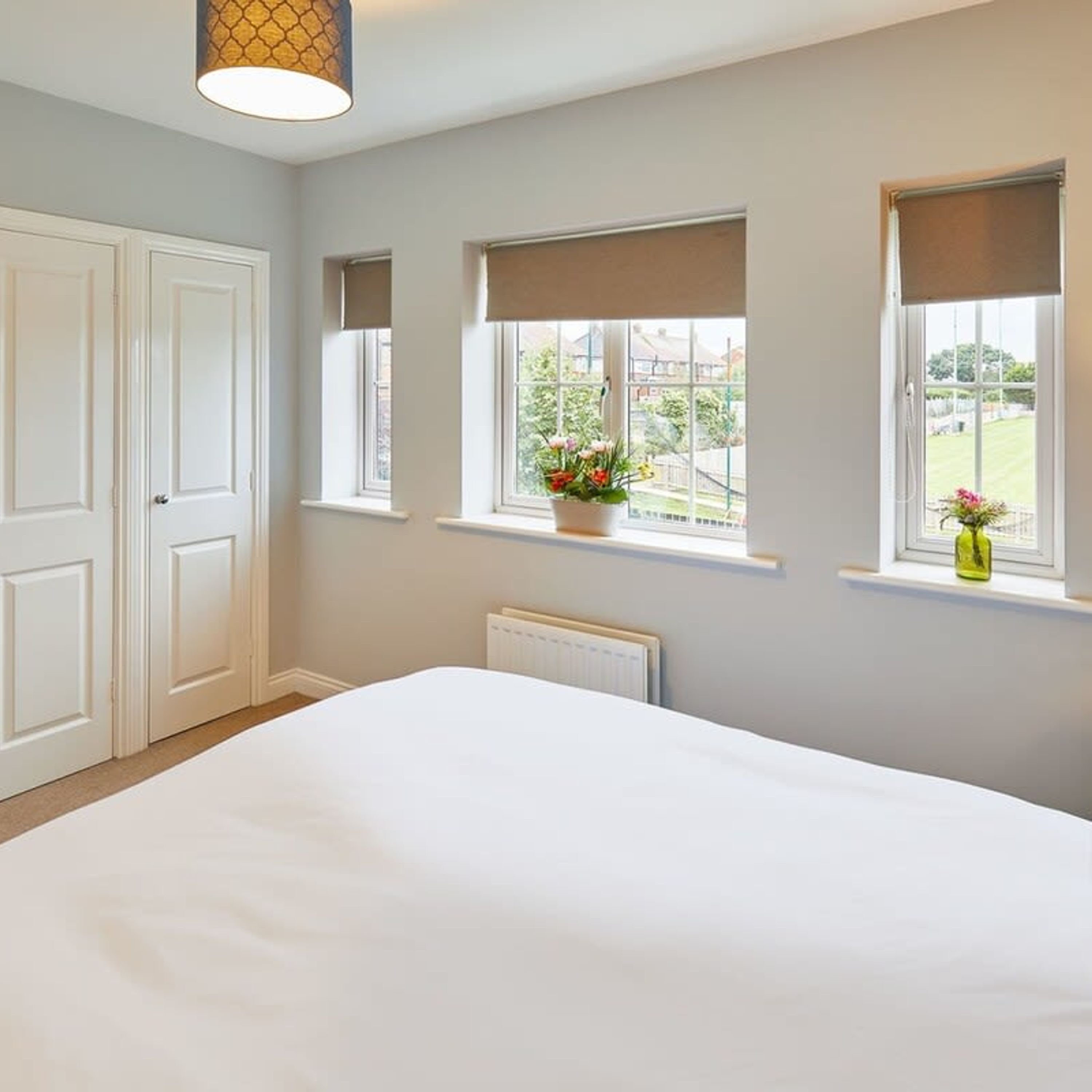 A bedroom with a large bed, two windows with curtains, a radiator, and a door.