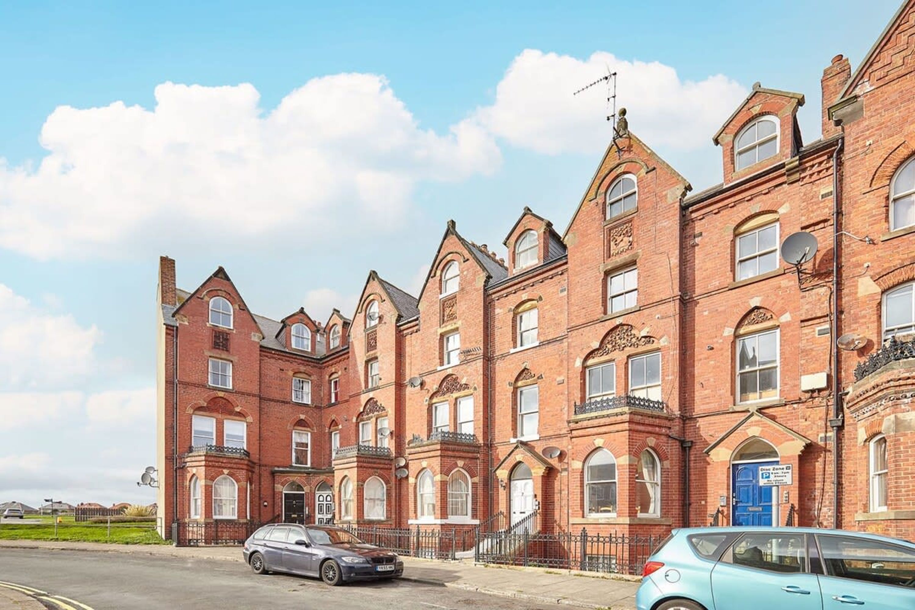 A row of red brick Victorian-style buildings with multiple windows and a blue door.