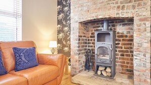 A living room with a brick fireplace, a leather sofa, and a floral wallpaper. - Host Stay Holmedene (Filey)