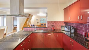 A modern kitchen with red cabinets, a stainless steel range hood, and a red tiled backsplash. - Host Stay Holmedene (Filey)