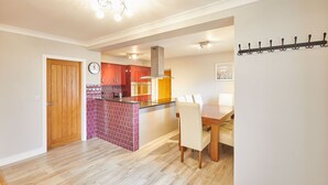 A modern kitchen with red cabinets, a brick backsplash, and a dining area with a wooden table and chairs. - Host Stay Holmedene (Filey)