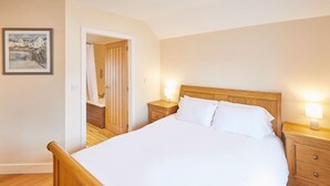 A bedroom with a wooden bed, white bedding, two bedside tables with lamps, a wooden wardrobe, and a framed picture on the wall. - Host Stay Holmedene (Filey)