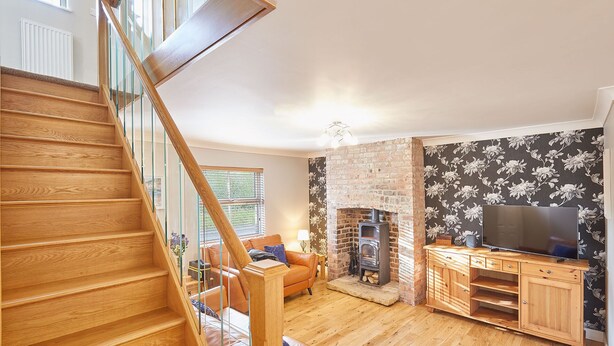 A wooden staircase leading to a living area with a fireplace, a television on a wooden cabinet, and a floral wallpaper pattern. - Host Stay Holmedene (Filey)