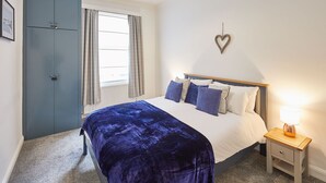 A bedroom with a bed, a nightstand, a lamp, a wardrobe, and a window with curtains. - Host Stay The Lookout (Scarborough)