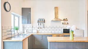 A modern kitchen with a central island, white tiled backsplash, stainless steel appliances, and a hanging pot rack. - Host Stay The Lookout (Scarborough)