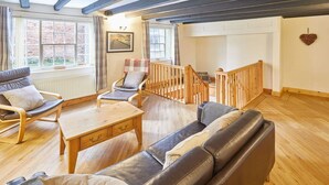 A cozy living room with a wooden staircase, leather sofas, and a view of the garden through large windows. - Host Stay Jacksons Cottage (Whitby)