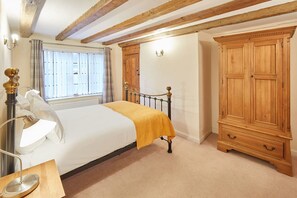A bedroom with a bed, bedside lamp, wooden wardrobe, and a window with curtains. - Host Stay Jacksons Cottage (Whitby)