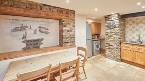 A cozy cottage kitchen with a wooden table and chairs, a stone wall, and a welcome sign. - Host Stay Jacksons Cottage (Whitby)