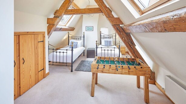A loft bedroom with a wooden ceiling, a bed, a futon, a foosball table, and a window. - Host Stay Jacksons Cottage (Whitby)