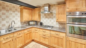 A kitchen with wooden cabinets, a stainless steel range hood, a microwave, a gas stove, and two ovens. - Host Stay Jacksons Cottage (Whitby)