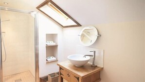 Ein Badezimmer mit Holzwaschtisch, weißem Waschbecken, rundem Spiegel und einem Oberlicht über dem Waschbecken.