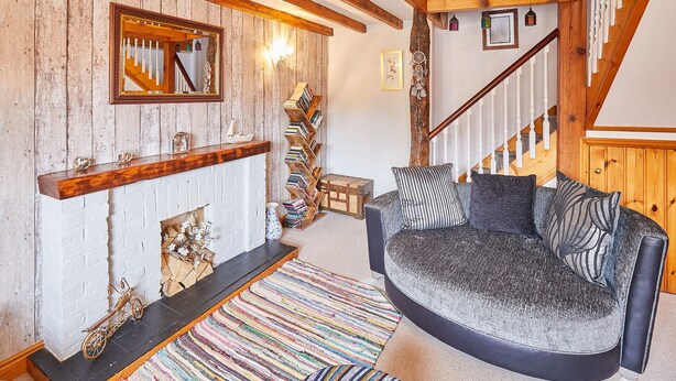 A cozy living room with exposed wooden beams, a fireplace, a bookshelf, and a colorful striped rug. - Host Stay Oldcorn Cottage (Whitby)