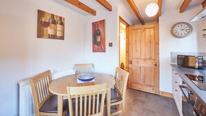 A dining area with a wooden table and chairs, a wall clock, and a door leading to another room. - Host Stay Oldcorn Cottage (Whitby)