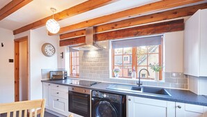 A kitchen with a washing machine, a sink, and a window with a view of a house. - Host Stay Oldcorn Cottage (Whitby)