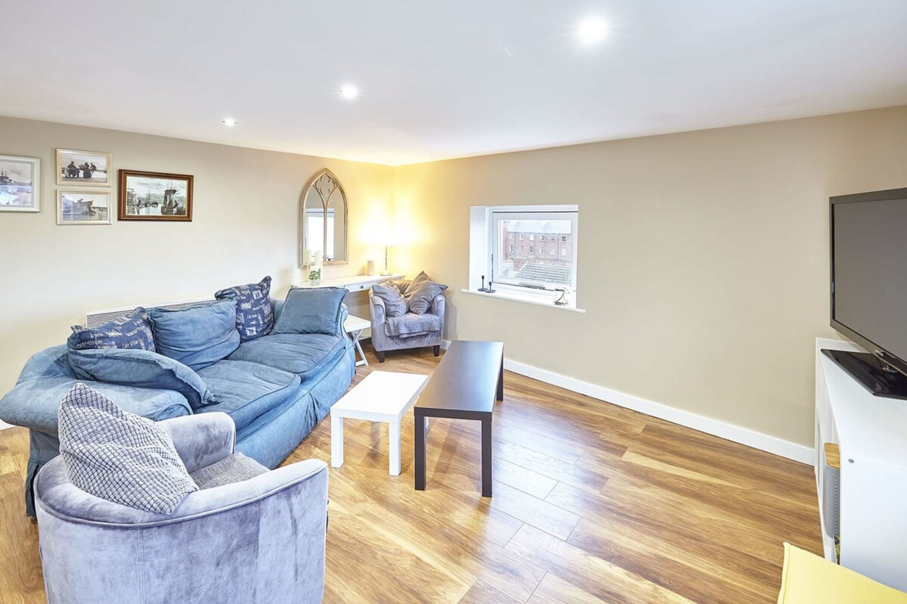 A living room with a blue sofa, a grey armchair, a white coffee table, and a TV on a white stand.