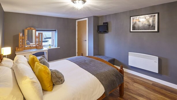 A bedroom with a bed, bedside table, mirror, dresser, and a television on the wall. - Host Stay Abbey Heights (Whitby)