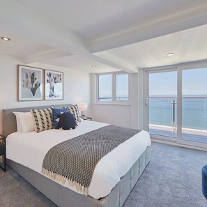 A modern bedroom with a large bed, two framed abstract artworks, a view of the sea through large windows, and a balcony. - Host Stay Penthouse Pier View (Whitby)