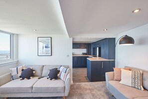 A modern living room with two sofas, a kitchen area, and a dining space. - Host Stay Penthouse Pier View (Whitby)