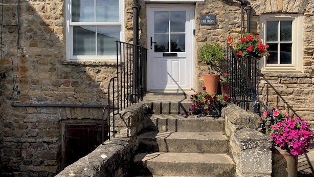 A stone building with a white door, a small window, and a sign that reads "The Old Dairy". - Host Stay The Old Dairy (Ripon)