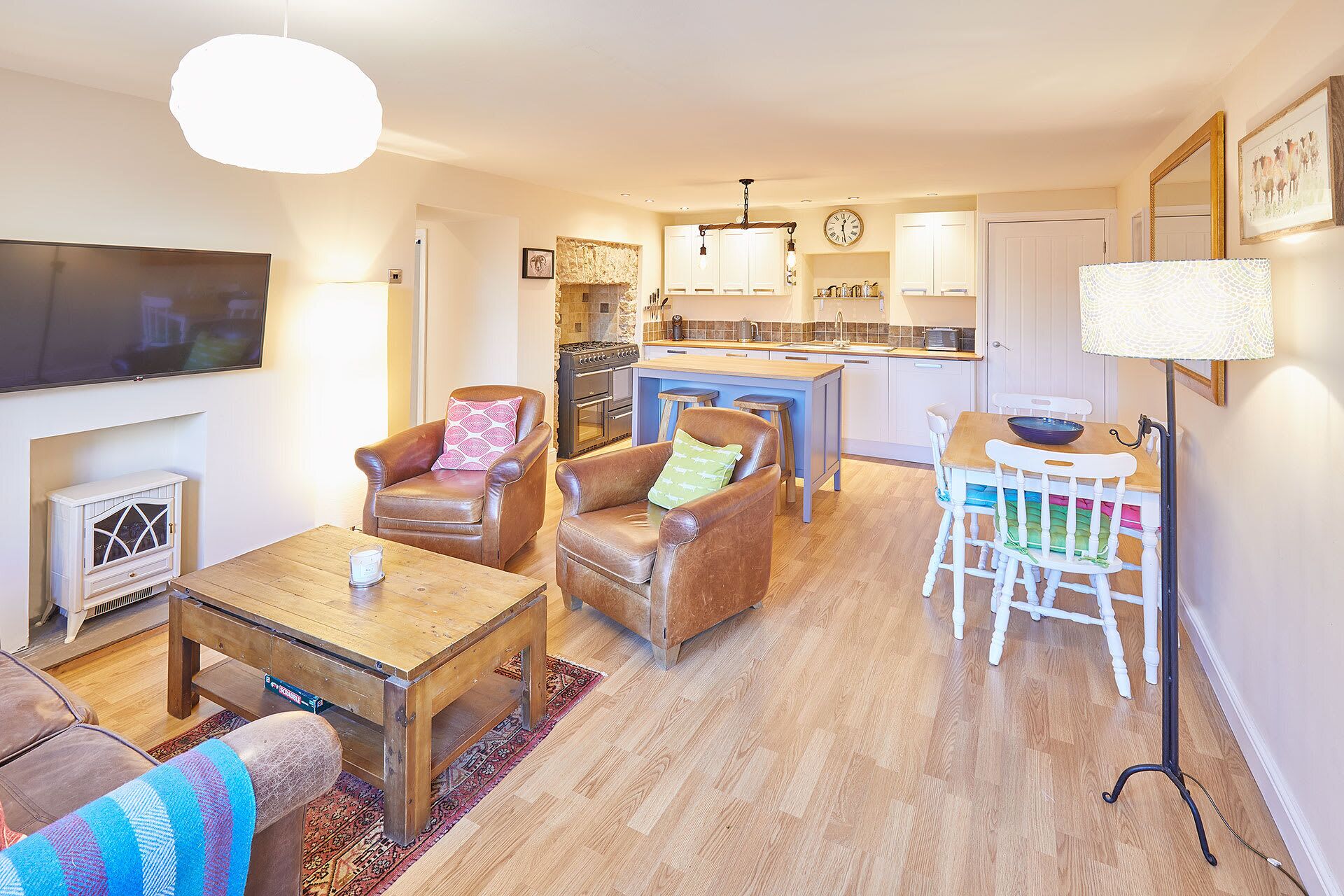 A living room with a TV, leather chairs, a wooden coffee table, and a kitchen area with a dining table and chairs.