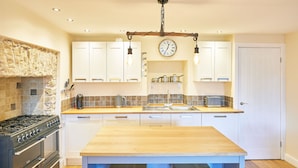 A modern kitchen with white cabinets, a wooden countertop, a built-in oven, and a hanging light fixture. - Host Stay The Old Dairy (Ripon)