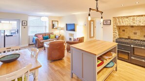 A modern kitchen with a built-in oven, a dining area with a wooden table and chairs, and a cozy seating area with a sofa and armchairs. - Host Stay The Old Dairy (Ripon)
