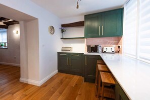 Une cuisine avec des meubles de couleur vert foncé, un plan de travail blanc et des tabourets en bois.