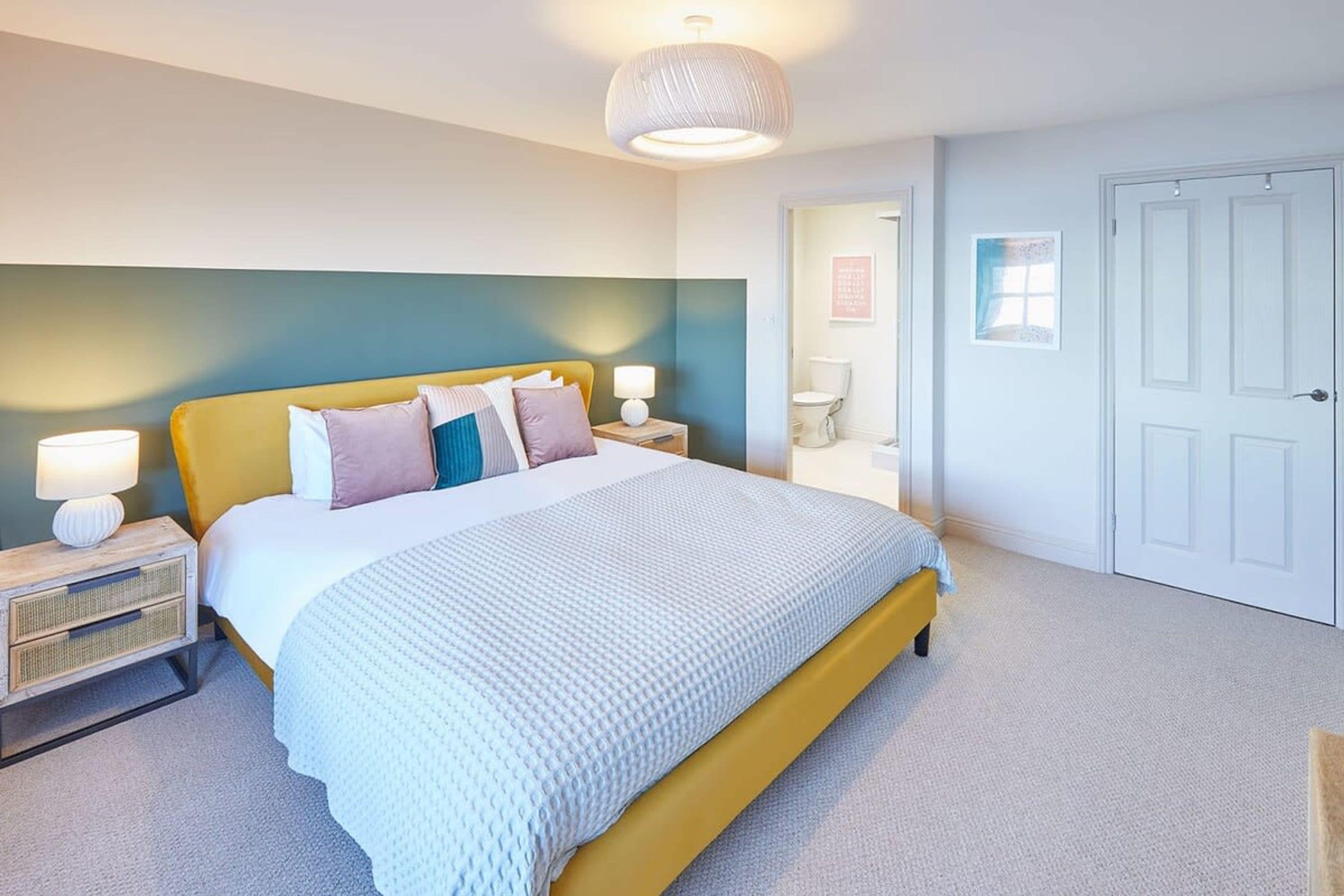 A bedroom with a bed, bedside tables, a lamp, a door, and a wall with a light switch.