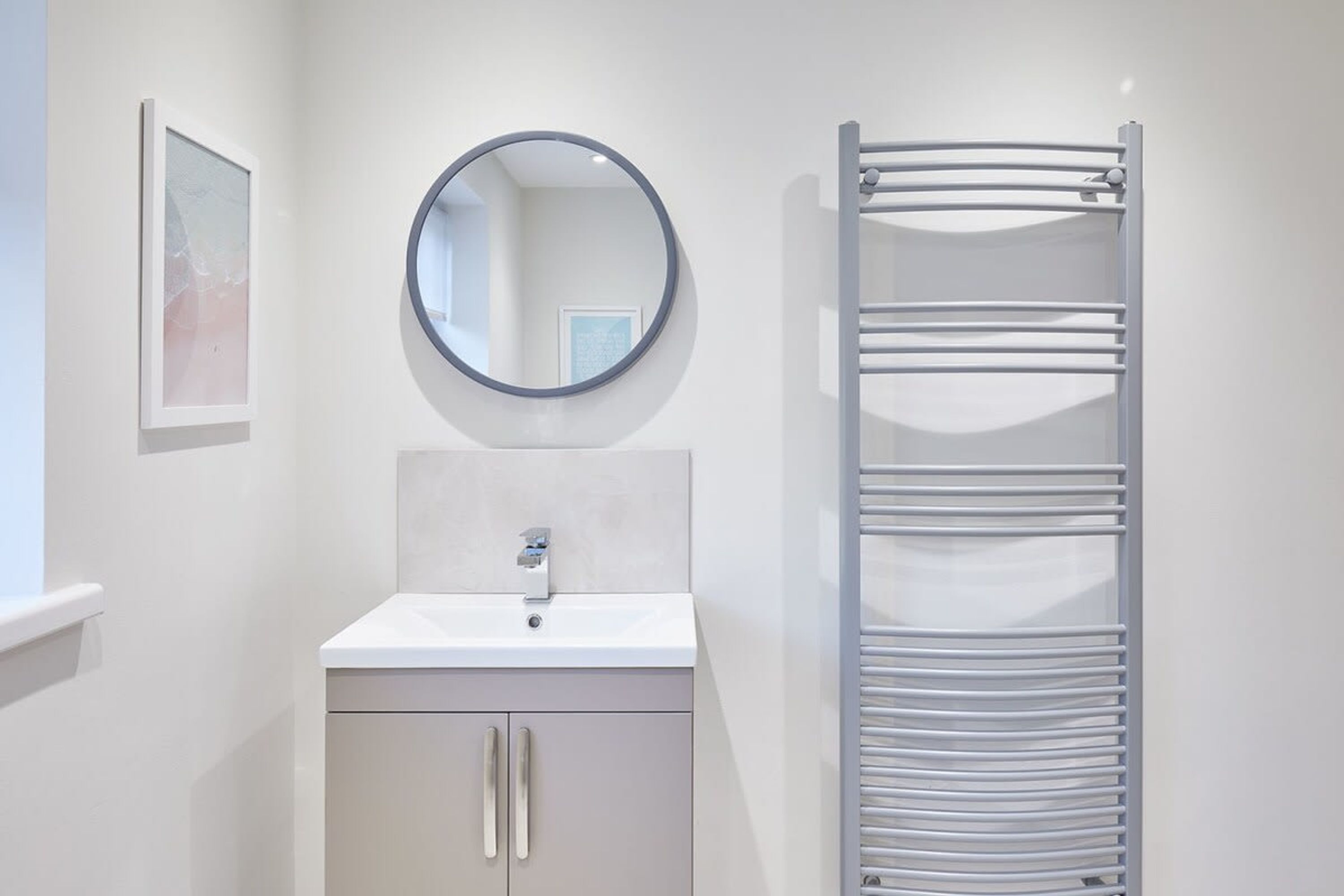 A bathroom with a white sink, a round mirror, and a towel rack.