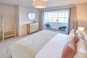 A bedroom with a bed, a dresser, a mirror, a window with curtains, a chair, and a small table.
