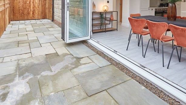 A modern patio with stone flooring, a wooden fence, and a glass door leading to an outdoor dining area with orange chairs and a table. - Host Stay Uggleby House Briggswath (Whitby)