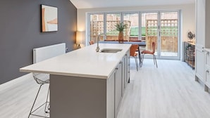 A modern kitchen with a central island, a dining area with chairs, and large windows offering a view of the outdoors. - Host Stay Uggleby House Briggswath (Whitby)