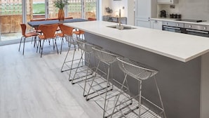 A modern kitchen with a large island, bar stools, and a dining area with orange chairs. - Host Stay Uggleby House Briggswath (Whitby)