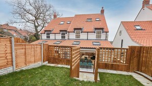 A two-story house with a tiled roof, a wooden fence, and a grassy yard. - Host Stay Iburn House Briggswath (Whitby)