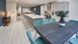 A modern kitchen with white cabinets, a central island, and a dining area with teal chairs. - Host Stay Iburn House Briggswath (Whitby)