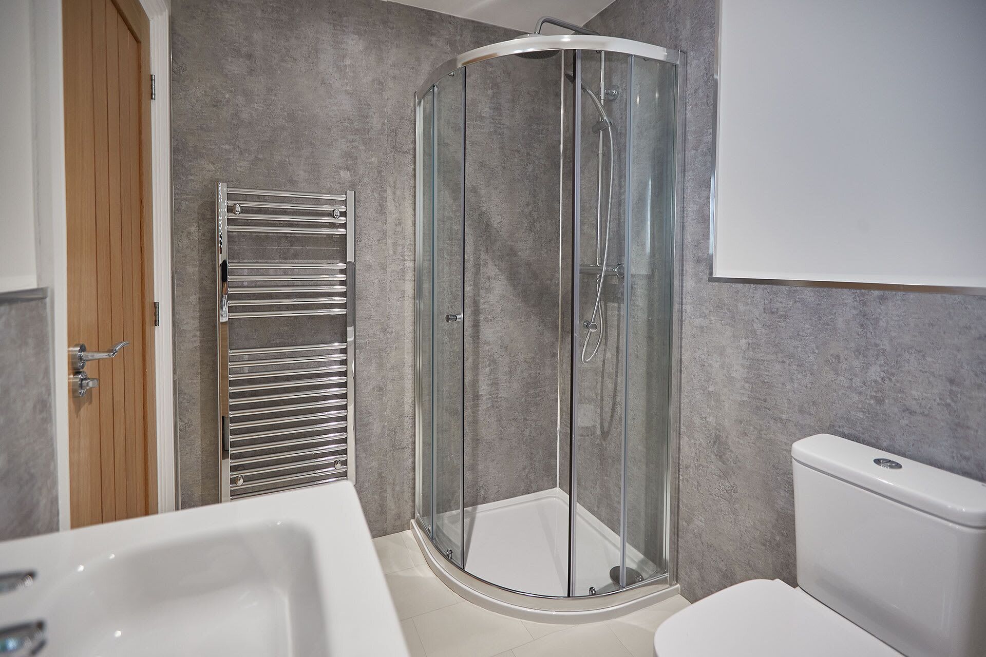 A modern bathroom with a glass-enclosed shower, a white toilet, and a built-in towel rack.