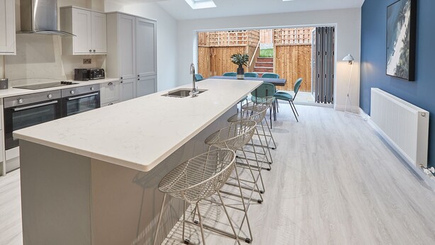 A modern kitchen with a large island, bar stools, and a view to a dining area with a wooden fence. - Host Stay Iburn House Briggswath (Whitby)