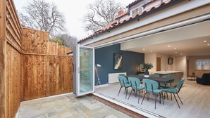 A modern kitchen with a large island, a dining area with teal chairs, and a wooden fence. - Host Stay Iburn House Briggswath (Whitby)