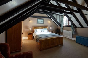 A bedroom with a sloped ceiling, a wooden bed, a nightstand, a chair, and a radiator.