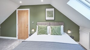 A bedroom with a sloped ceiling, a wooden door, a framed picture on the wall, a bed with green and white pillows, two bedside lamps, and a grey carpet. - Host Stay Littlebeck House Briggswath (Whitby)